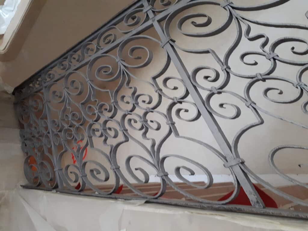 Décapage d'une rampe d'escalier en fer forgé avec des motifs décoratifs complexes.