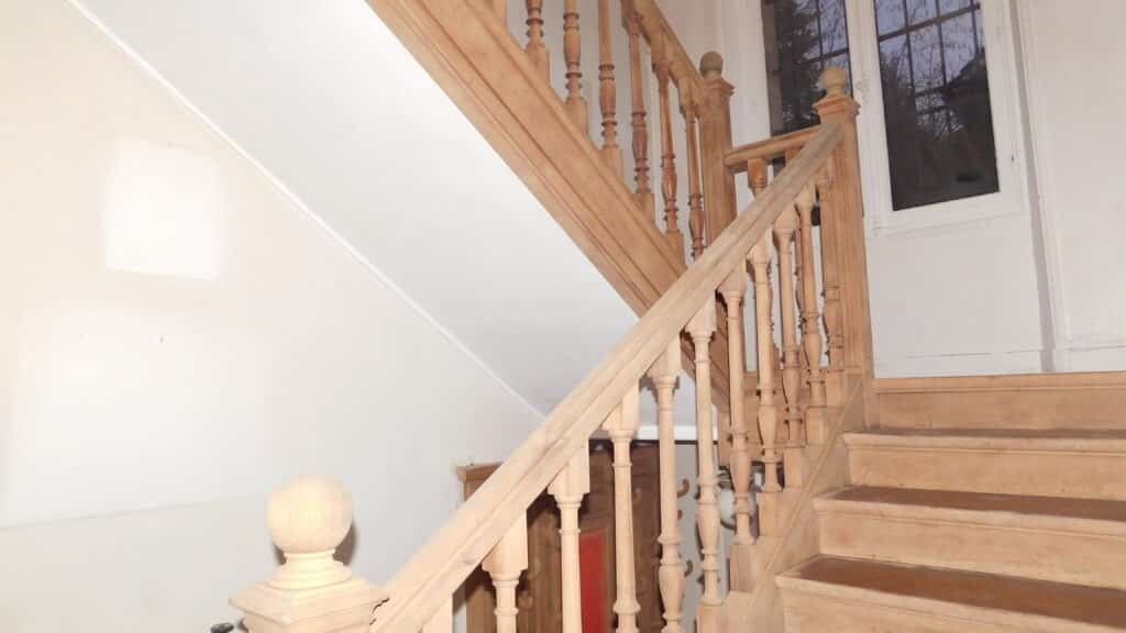 Décapage d'un escalier intérieur en bois avec une rampe ornée de balustres, dans un environnement lumineux.